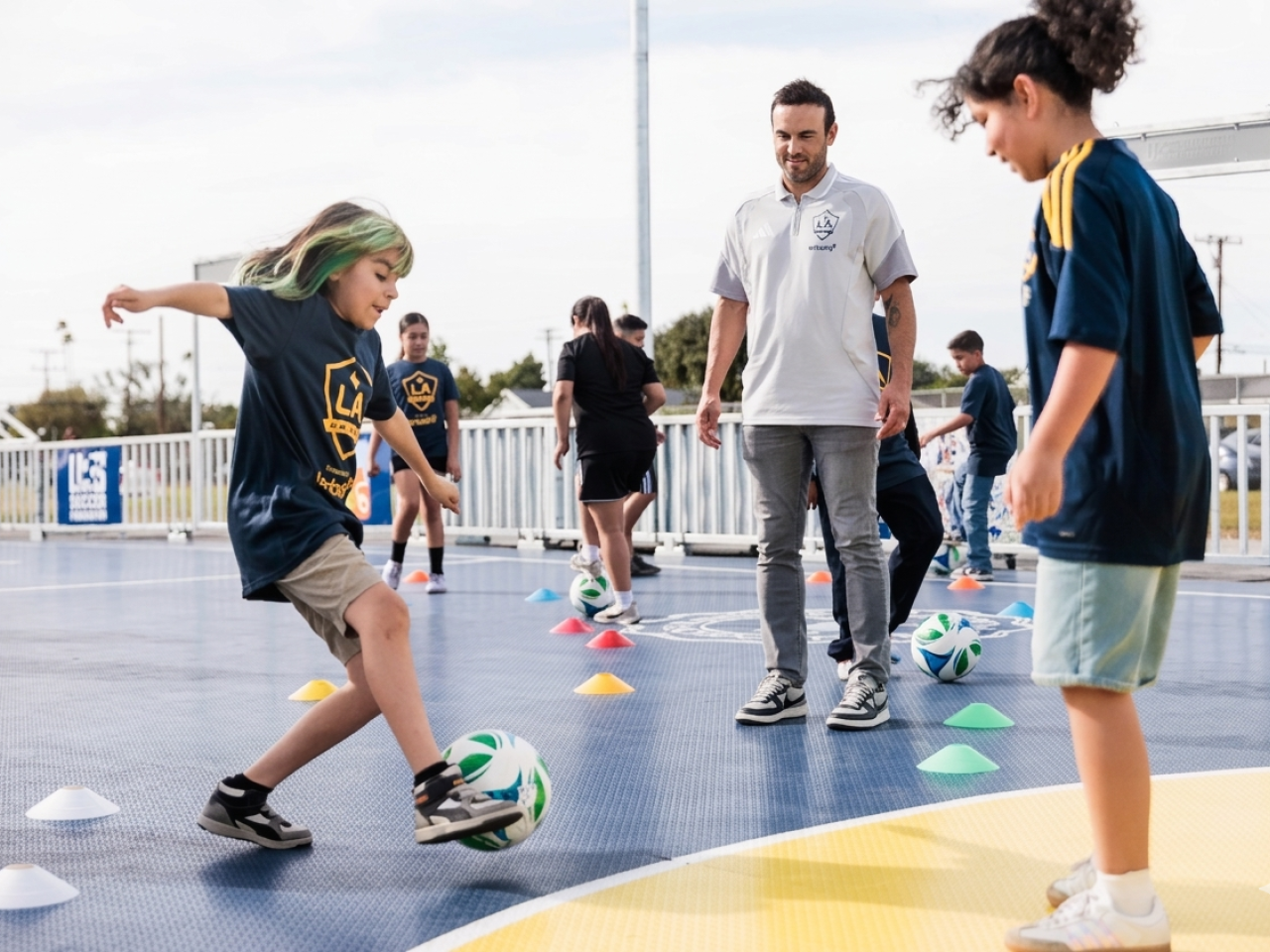 Landon Donovan watching a student practice soccer drills on a mini-pitch.