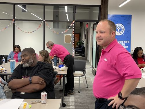 Someone in a pink shirt standing up amongst others seated at desks