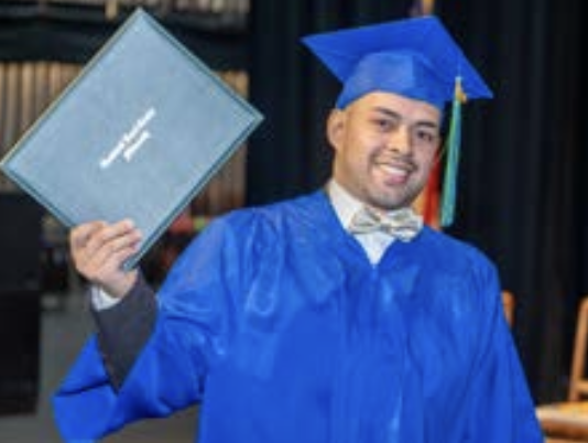 Man in graduation cap & gown with diploma