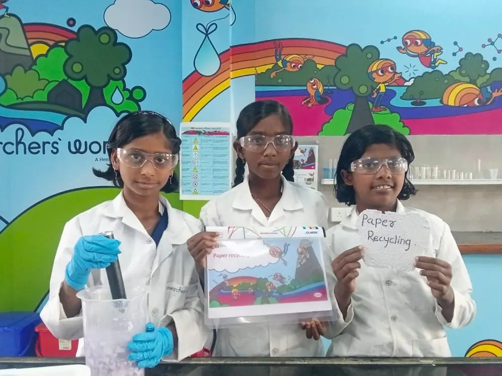 Three students in white coats posing in front of a colorful mural