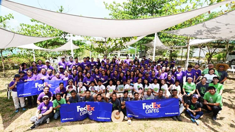 Large group posed under shade canopies with FedEx Cares banners