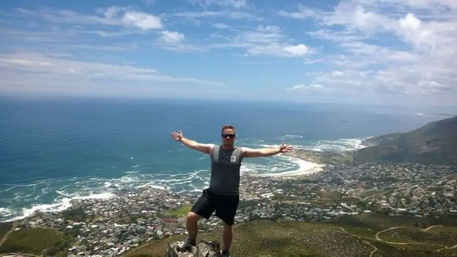 Kevin McMenamin holding out arms at the top of a mountain