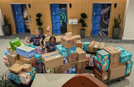 Two people waving from among a large pile of boxes
