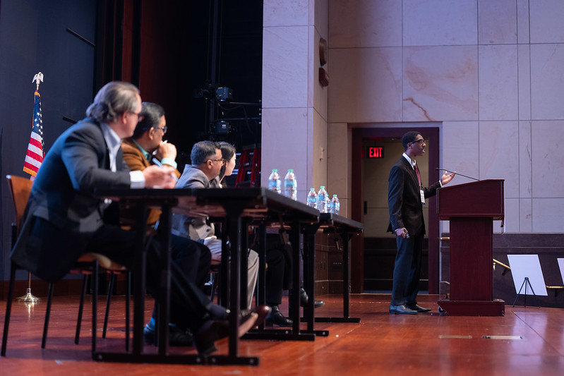 Speaker at lectern and with a panel sitting nearby