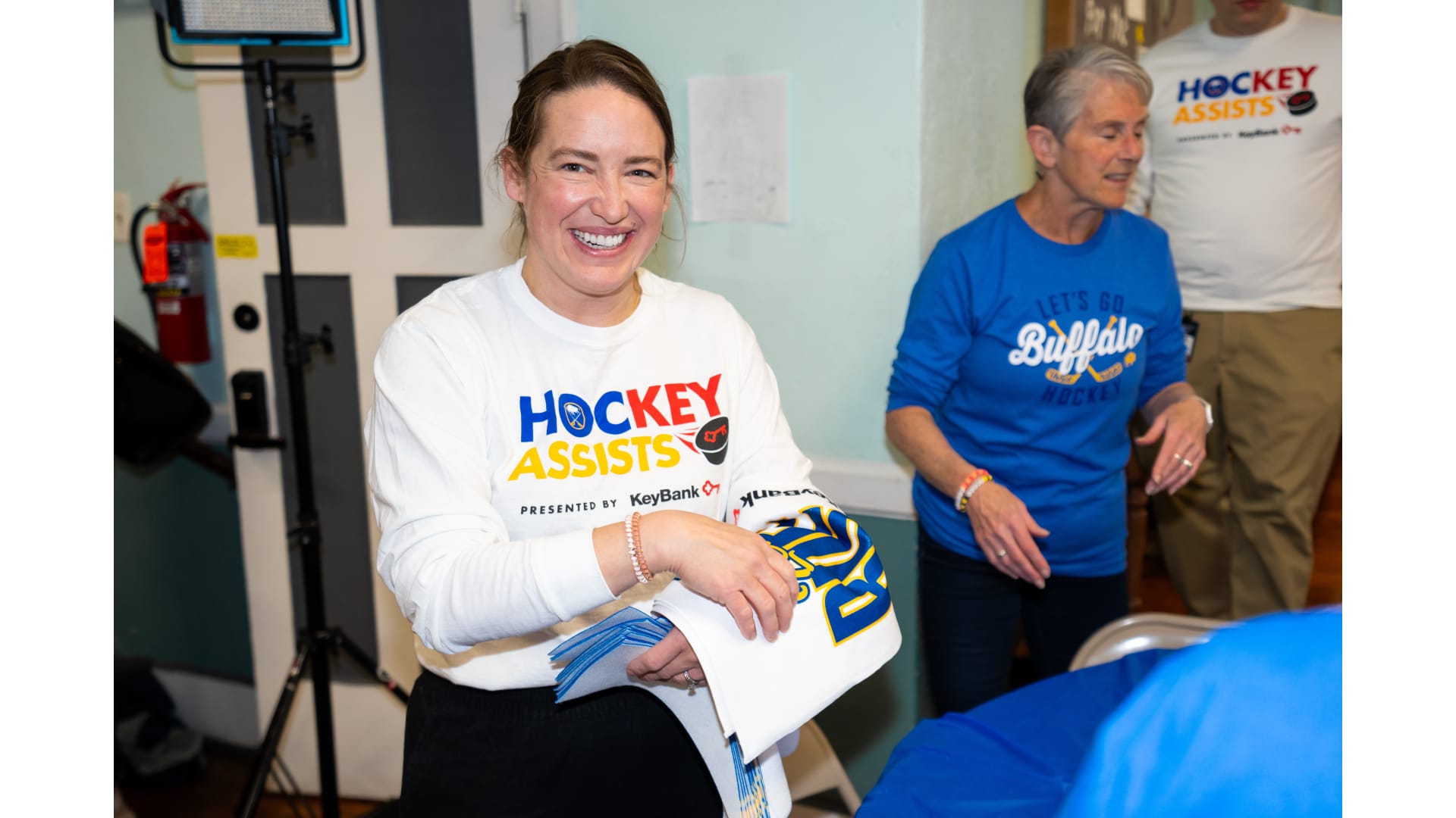 A smiling person in a "Hockey Assists" t-shirt