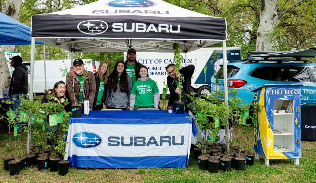 Volunteers with potted trees under a Subaru tent