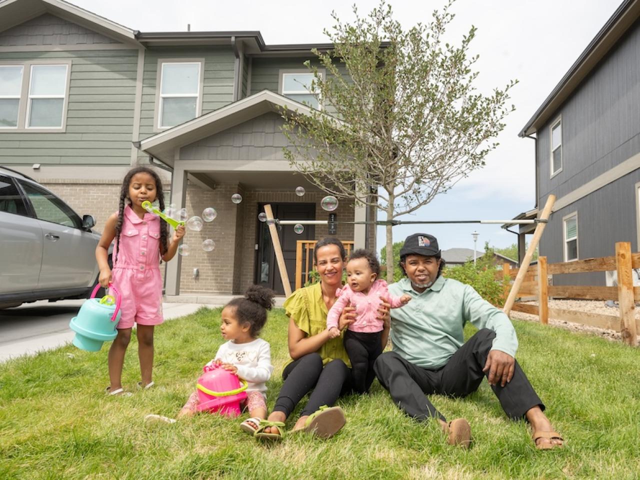 Family of parents and three children sitting in front of house blowing bubbles