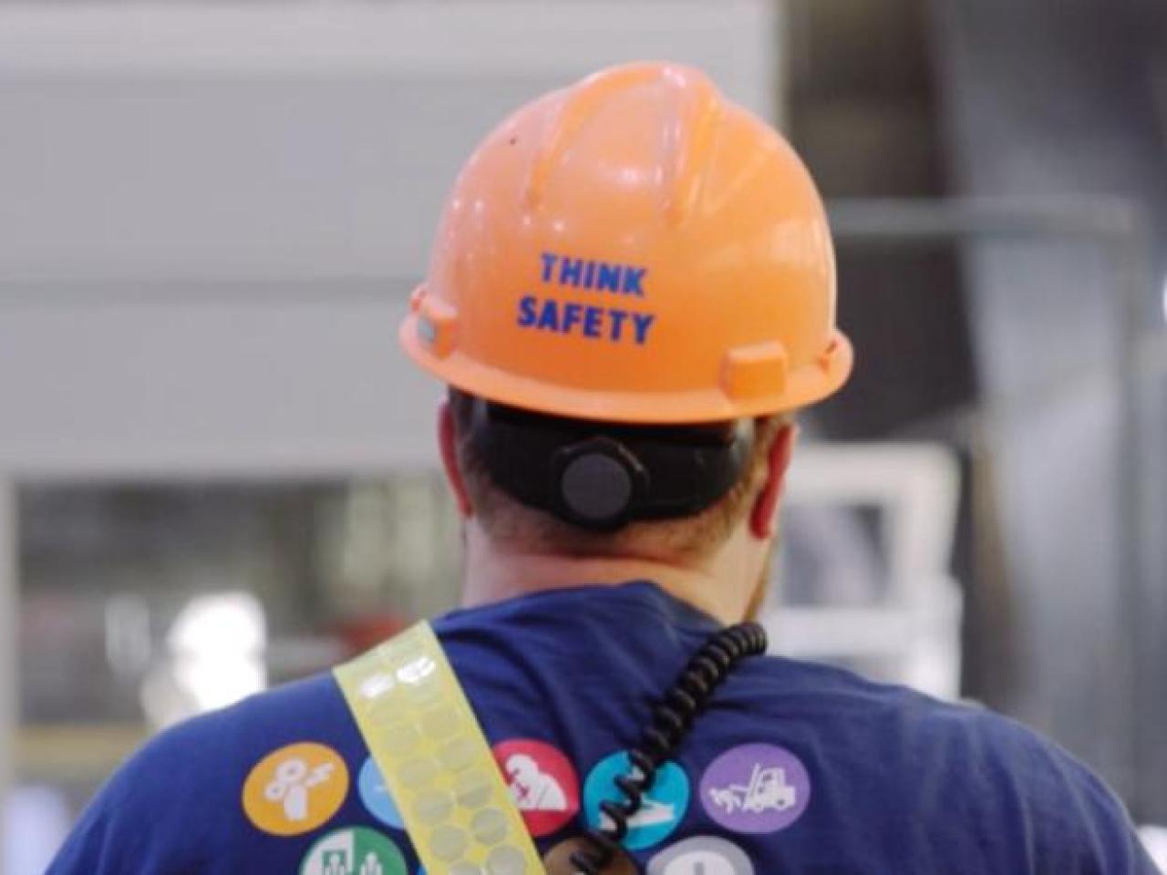 A person walking away, "Think Safety" on the back of their hard hat.