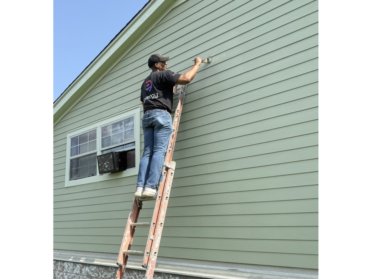 Volunteer on a ladder painting a house exterior