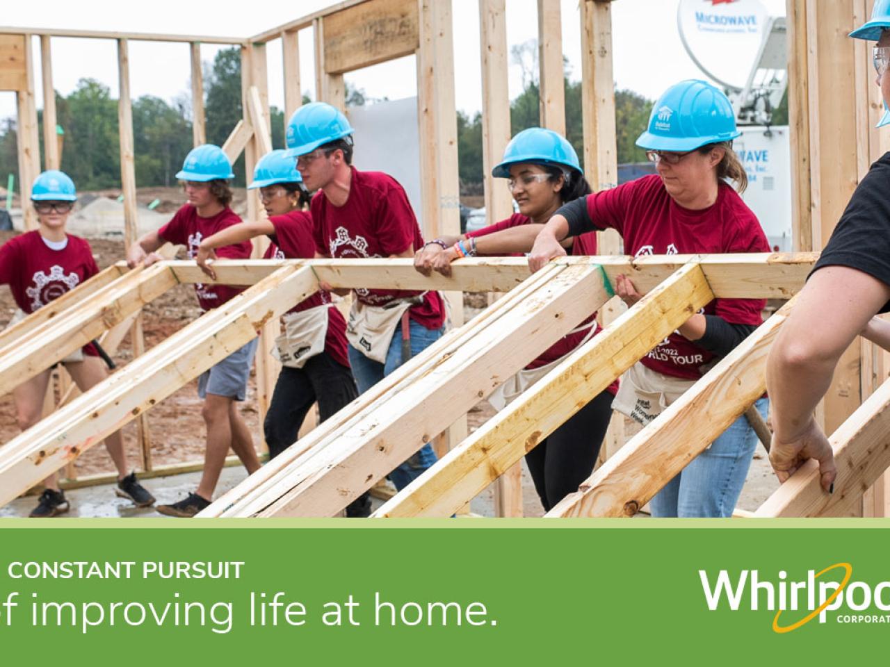 Volunteers lifting up framing for a house with text "In constant pursuit of improving life at home" with the Whirlpool logo