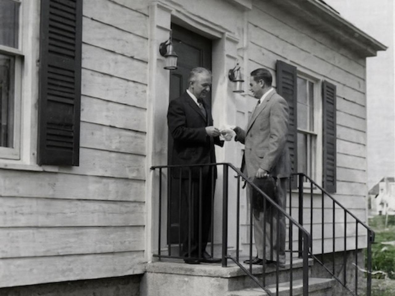Webster Bank Founder Harold Webster Smith (pictured right with hat in hand) delivers the bank’s first loan to Joe Baltrush in December 1935 on the steps of his home at 114 Chambers Street in Waterbury.