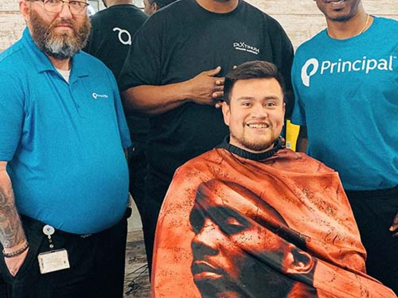 Jonas Cutler seated in a barber chair with three men standing behind him.