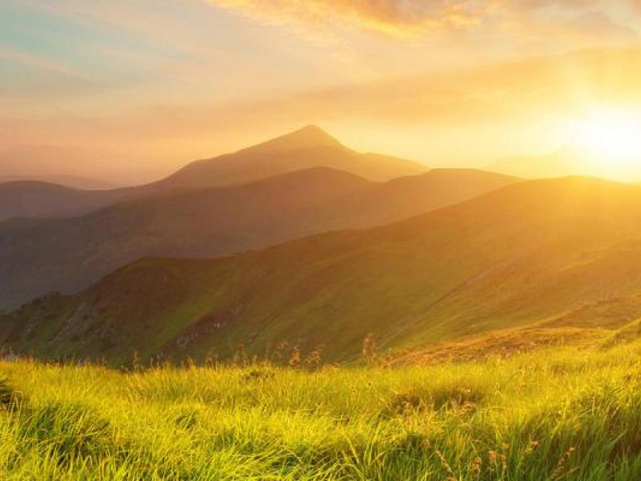 A sunset over mountain range with grassy plains.