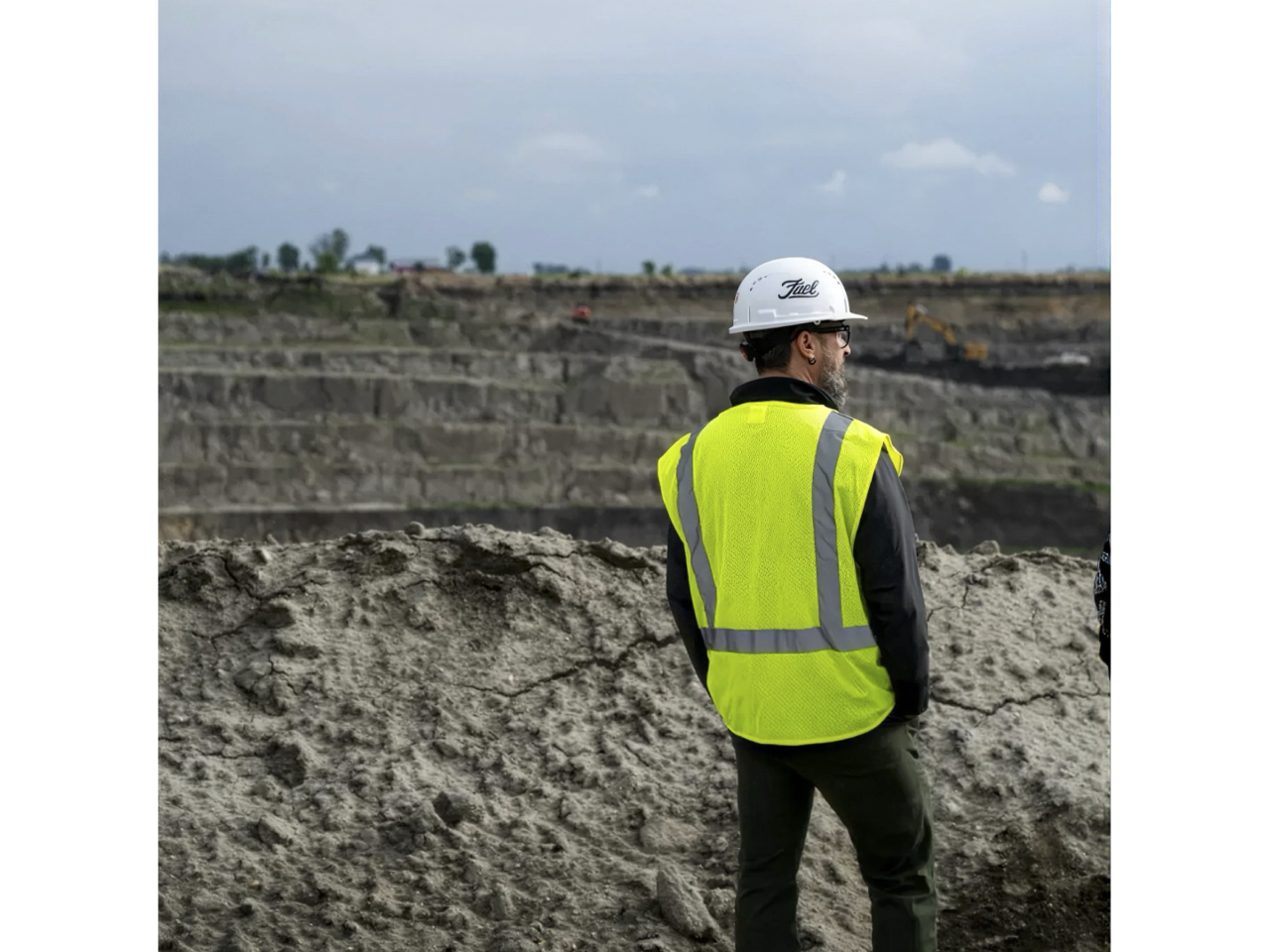 Man in hard hat and yellow vest looking out over mining site