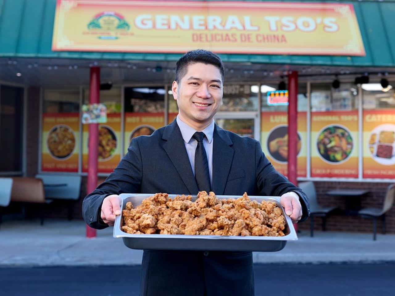 Someone holding up a tray of chicken in front of a restaurant