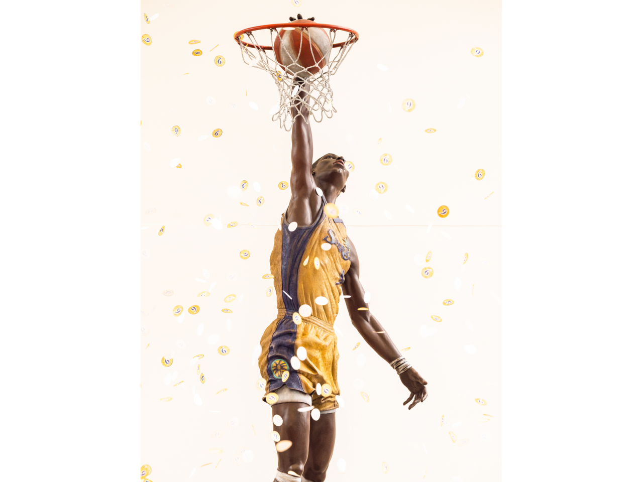 Close-up view of bronze Los Angeles Sparks basketball player Lisa Leslie statue reaching through the hoop as gold confetti falls around it.