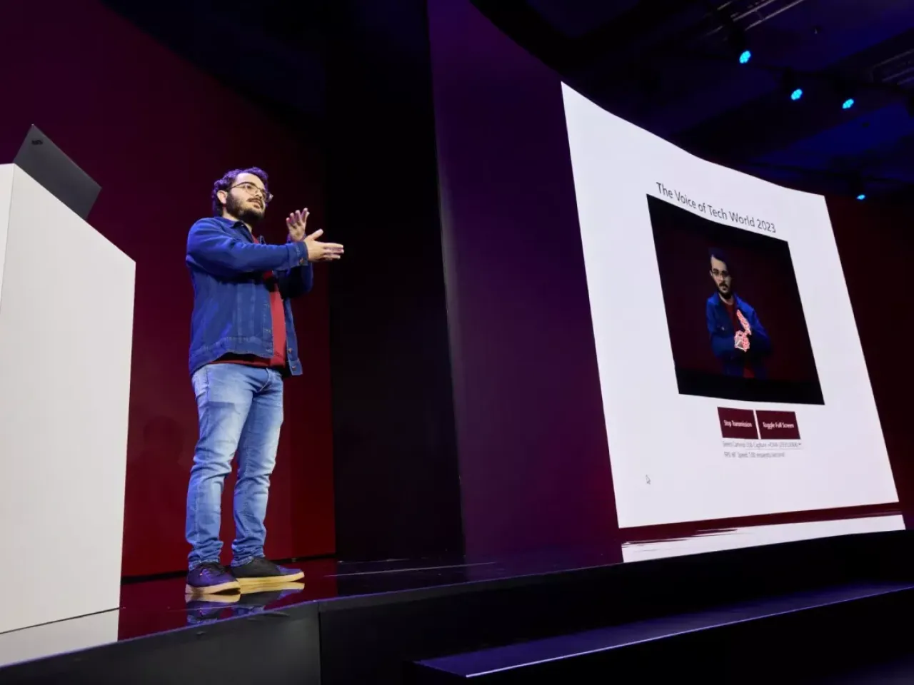 Gabriel presenting on stage using sign language and a digital display.