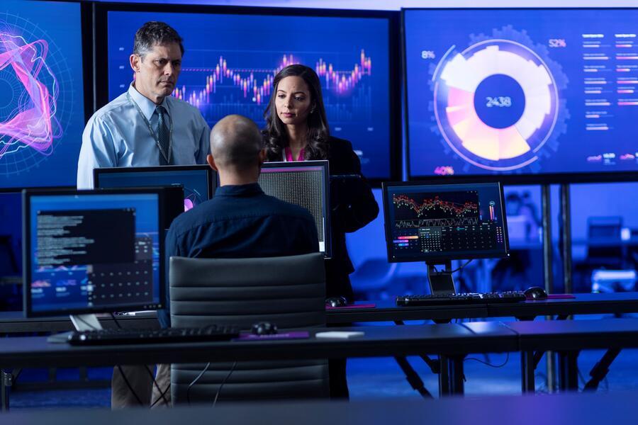 Three people working amongst many computer screens