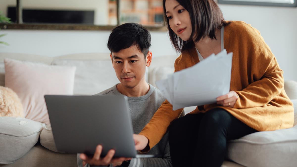 Two people looking at sheets of paper and computer screen toghether