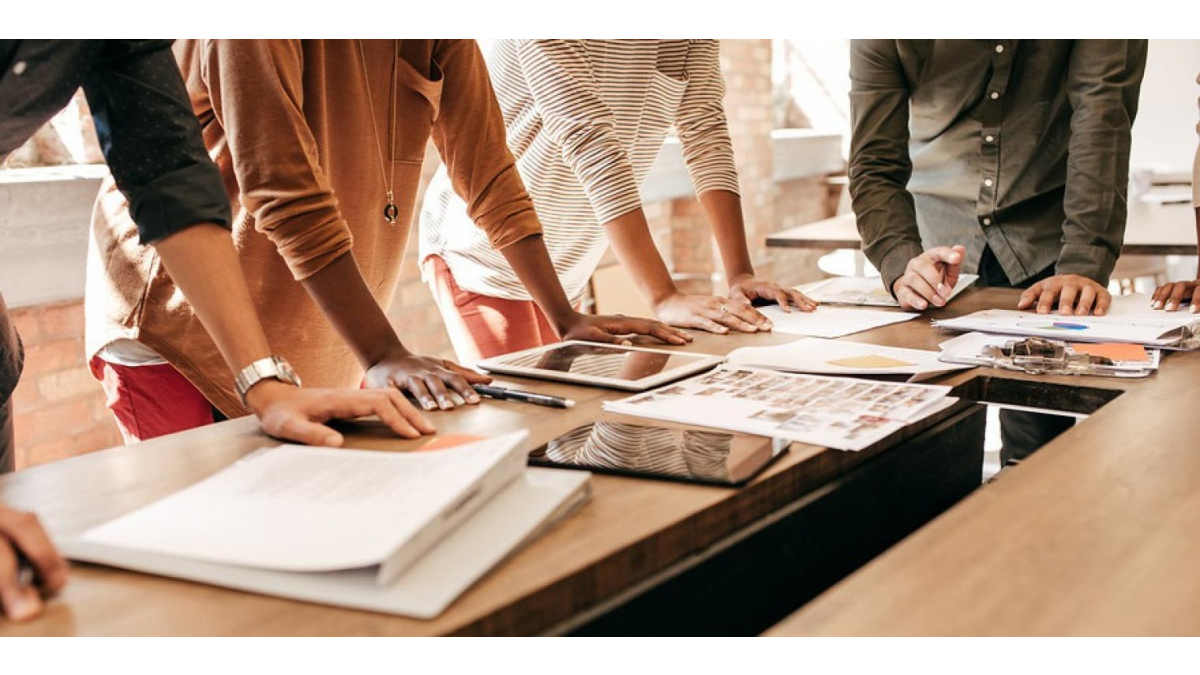 Four individuals leaning over a desk with papers on it