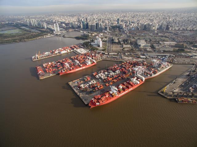 Aerial view of DP World’s Buenos Aires terminal on the Río de la Plata, showing container ships docked at the port with the city skyline in the background.