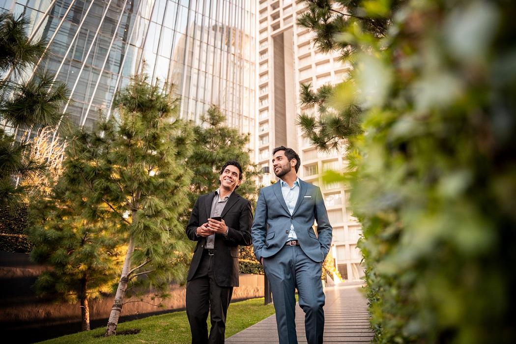 two people talk beside tall buildings and trees