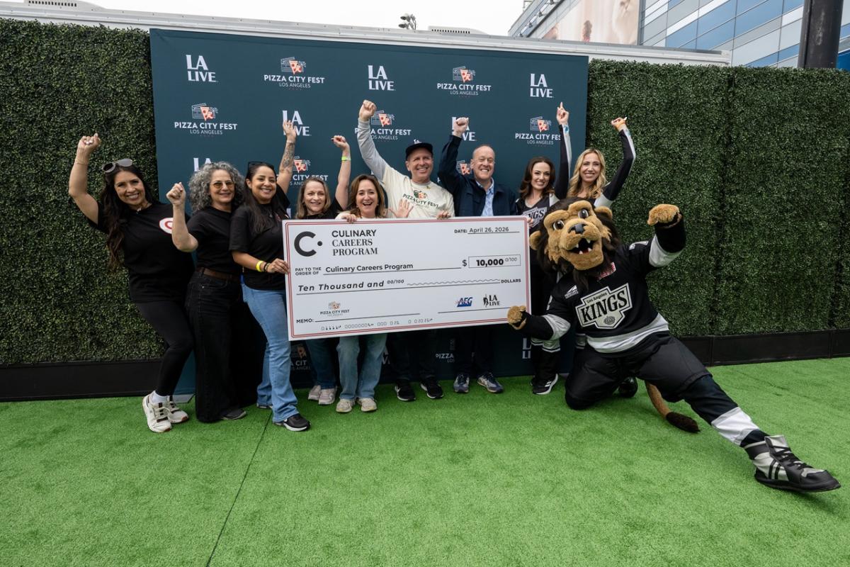 Group stands on a branded step-and-repeat holding a large donation check for the Culinary Careers Program at LA LIVE, with a mascot posing nearby.