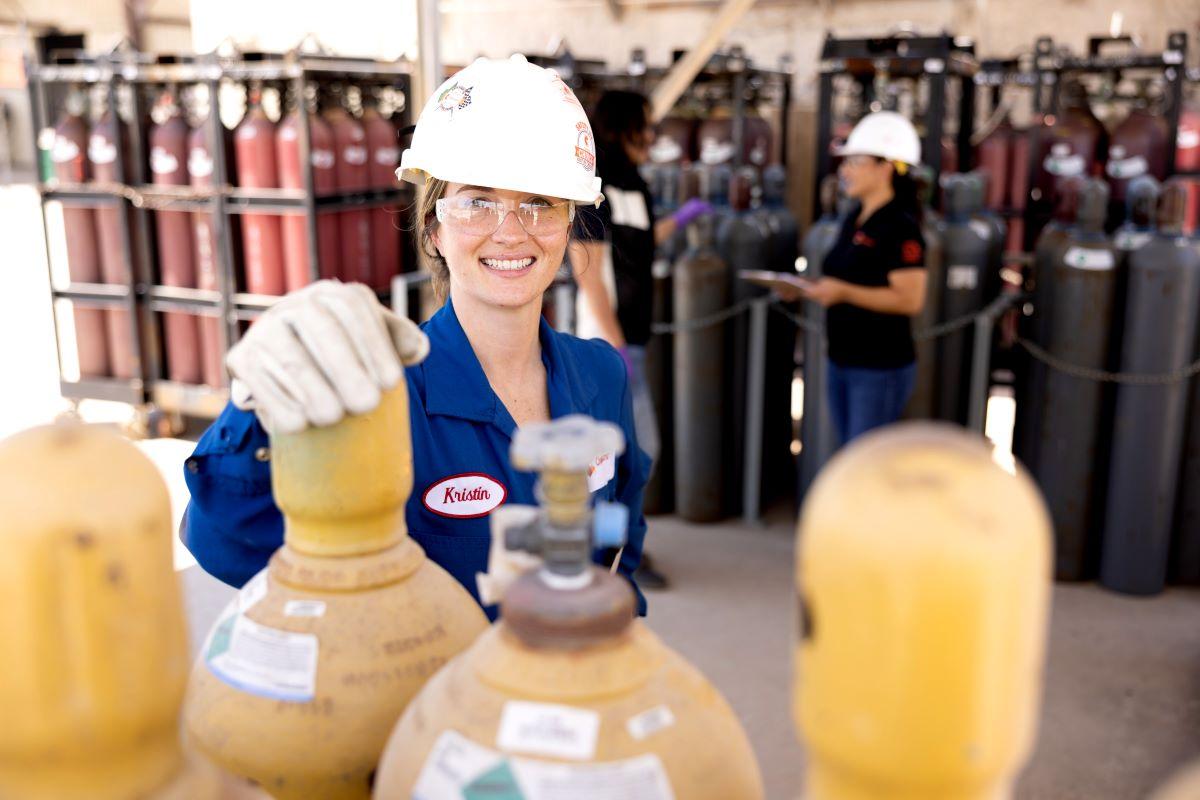 workers in hard hats and protective wear standing with groups of tall metal cylinders.
