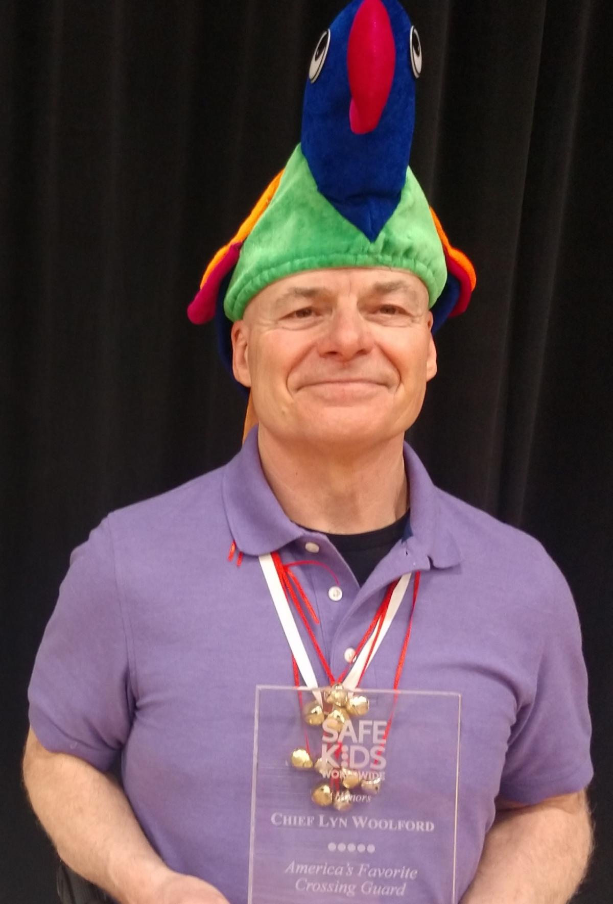A man in a purple polo and novelty hat holding an award