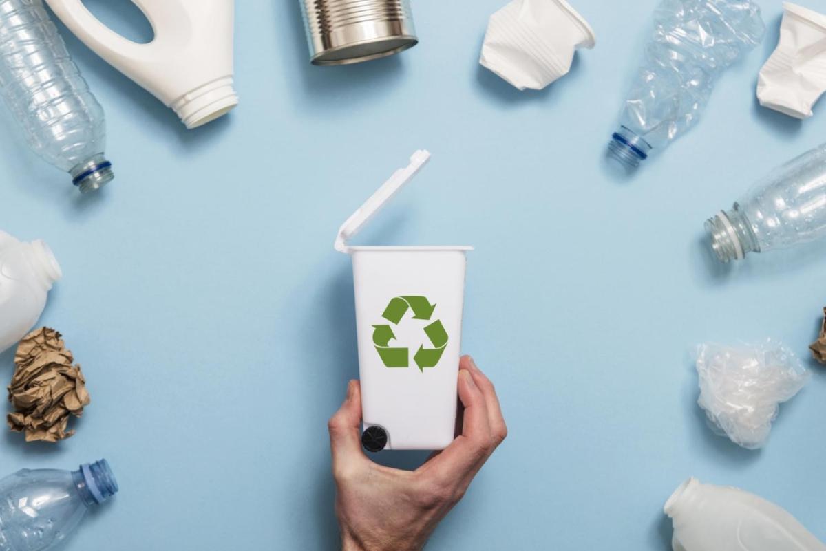 a hand holding a small recycling bin surrounded by plastic bottles