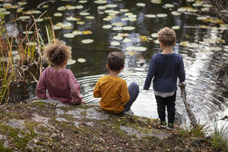 Three children sitting by a stream.