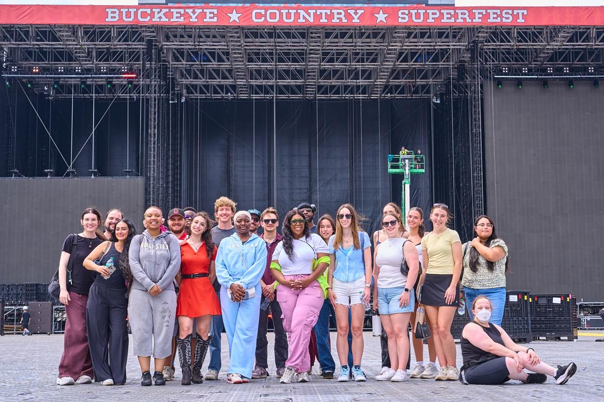 College program participants pose for a group photo in front of the main stage at Buckeye Country Superfest, standing on the festival grounds before the event begins.