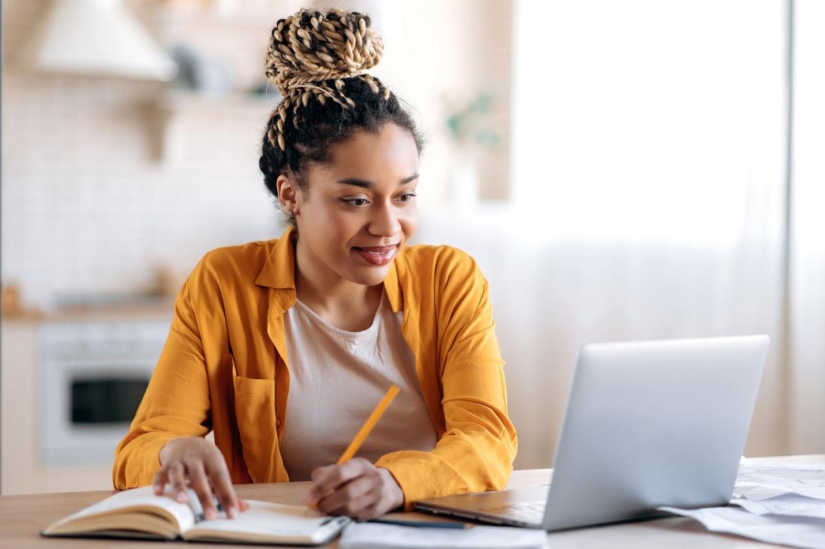 Person writing in notebook while looking at laptop screen