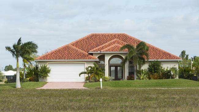 Palm trees and lawn in front of a stucco house with a red tiled roof.