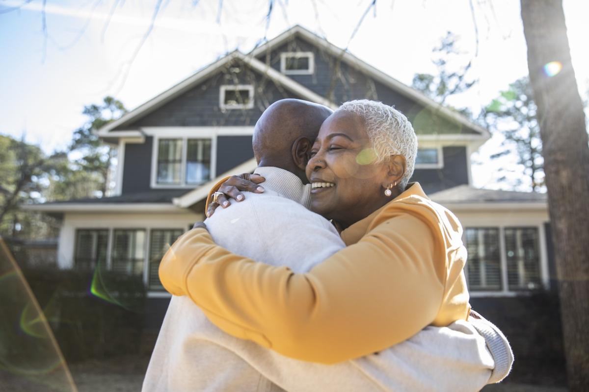Older couple hugging outside of their new home.