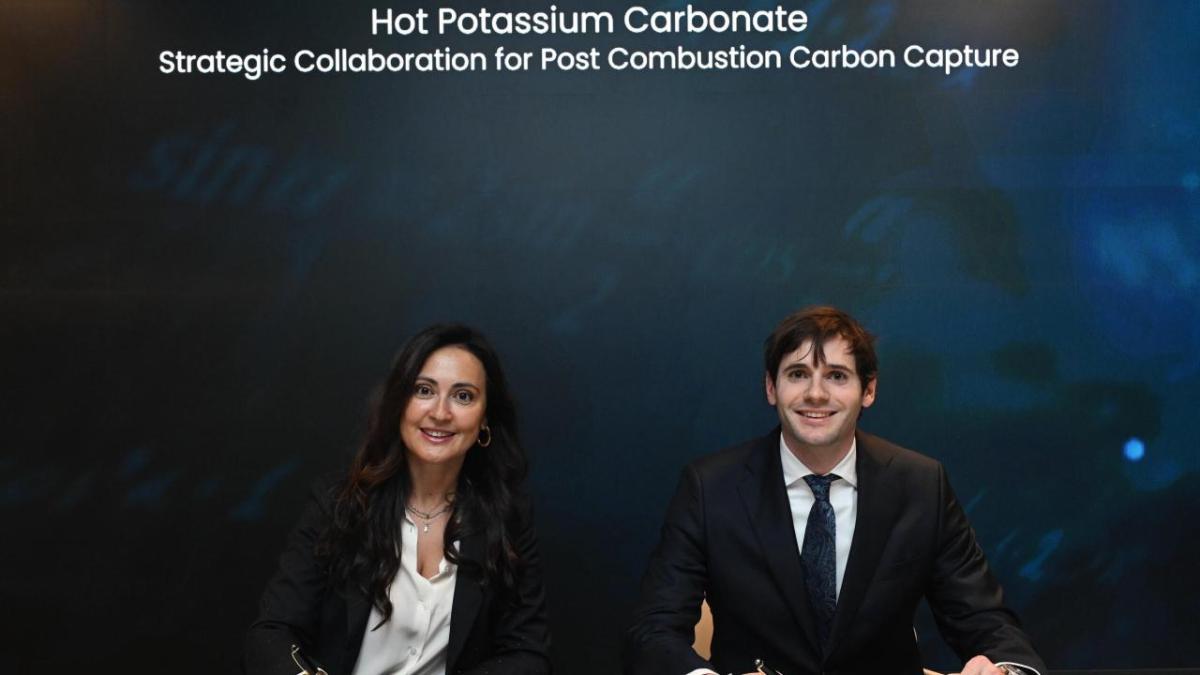 Two smiling business people sitting under the words, "Hot Potassium Carbonate Strategic Collaboration for Post Combustion Carbon Capture"
