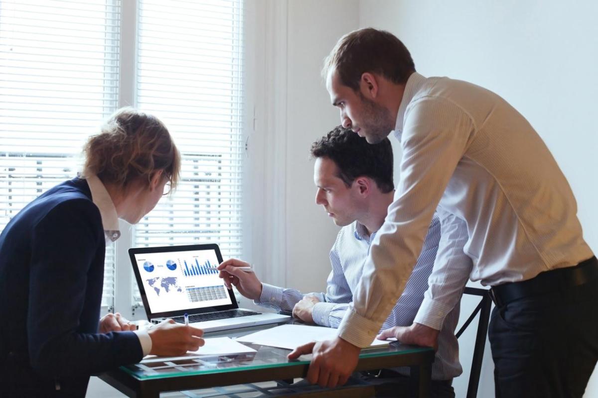 Three coworkers gathered around a computer displaying data visualizations