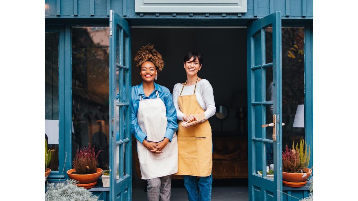 Two women wearing aprons at entrance of business