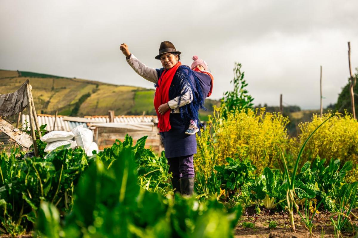 farmer stands in a field her baby strapped to her back
