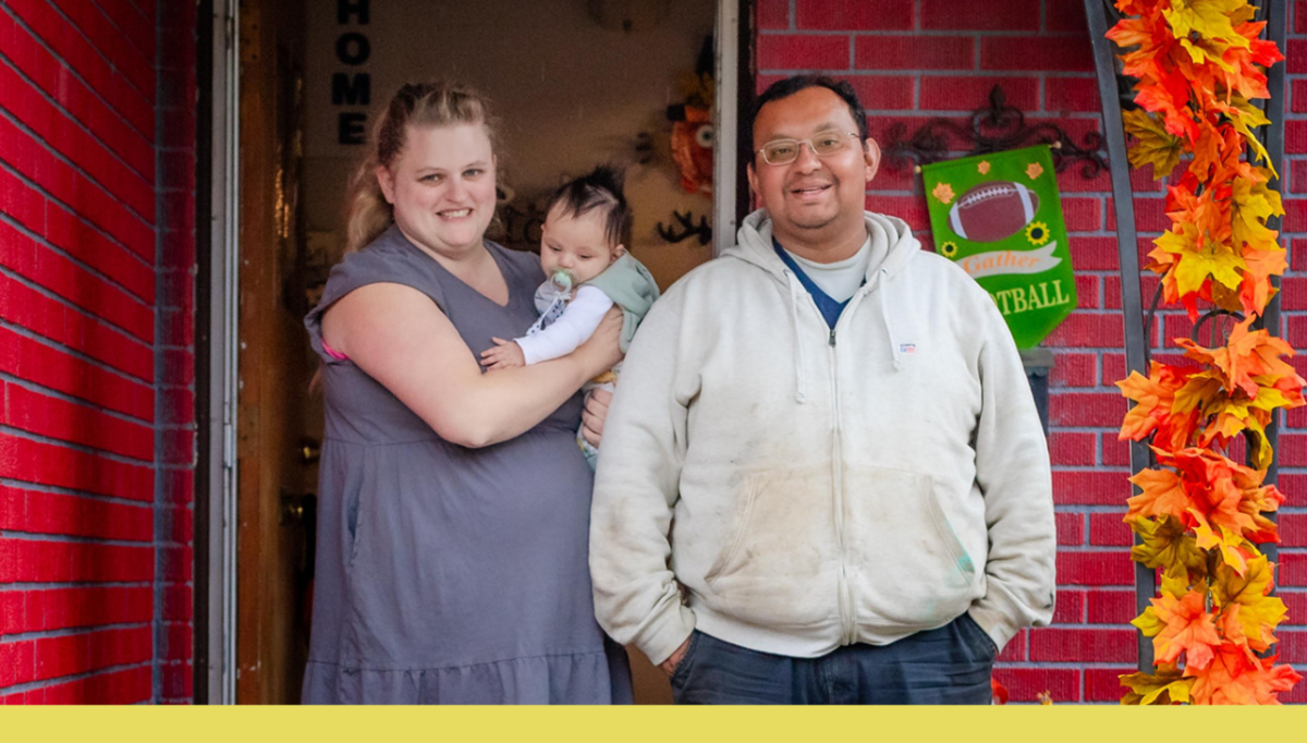 A smiling couple on their porch holding a baby
