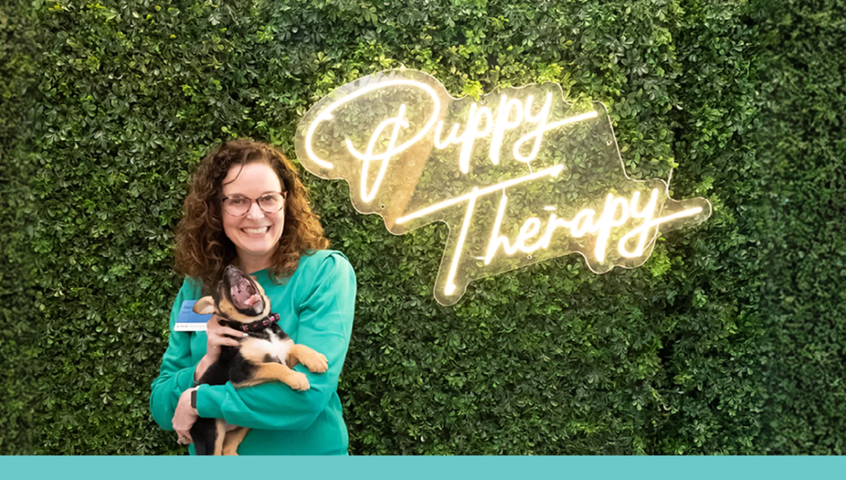 Woman holding dog with the words, "Puppy Therapy" behind them
