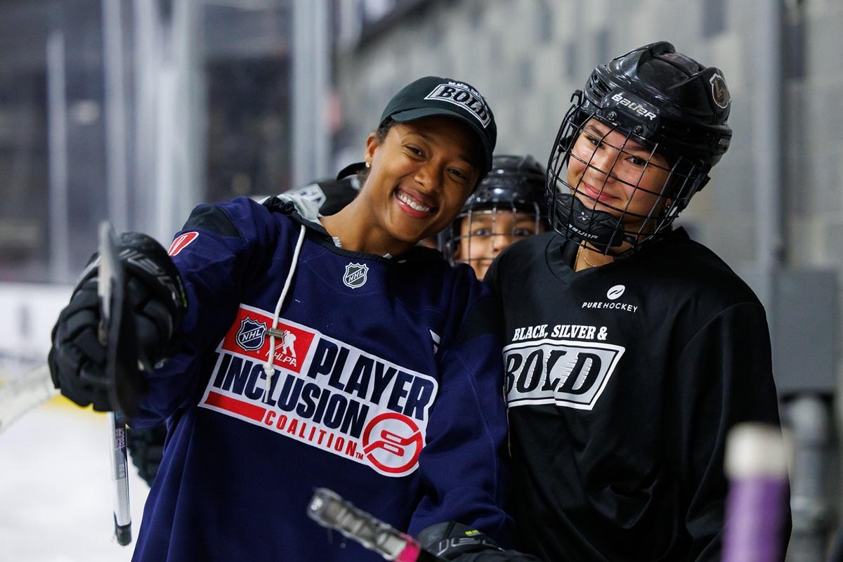 Blake Bolden in a Player Inclusion Coalition jersey poses with a participant in Black, Silver & Bold gear during a hockey clinic.