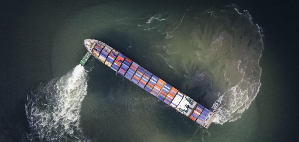 Two small boats moving a container vessel.