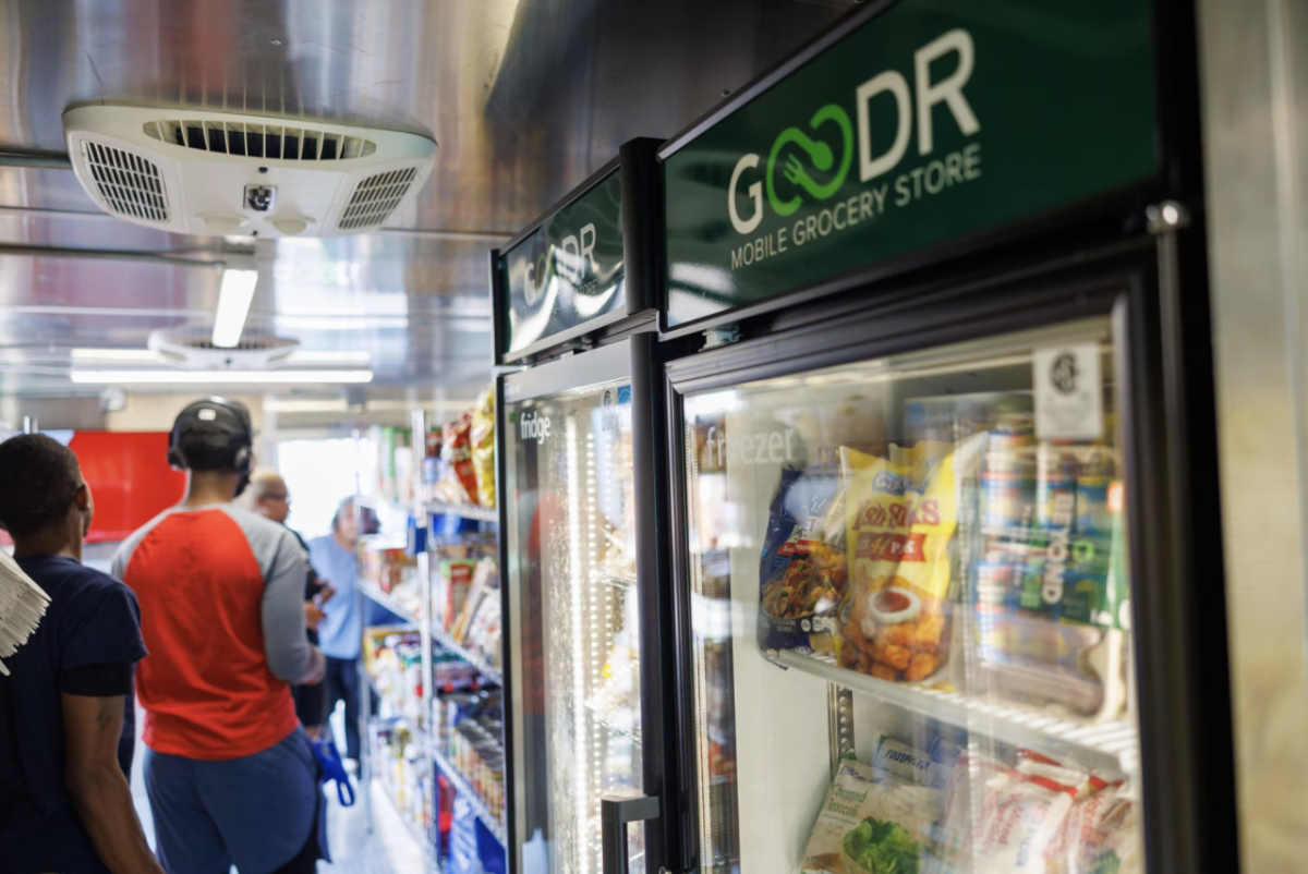 People in a line past a Goodr labeled fridge in a mobile grocery store
