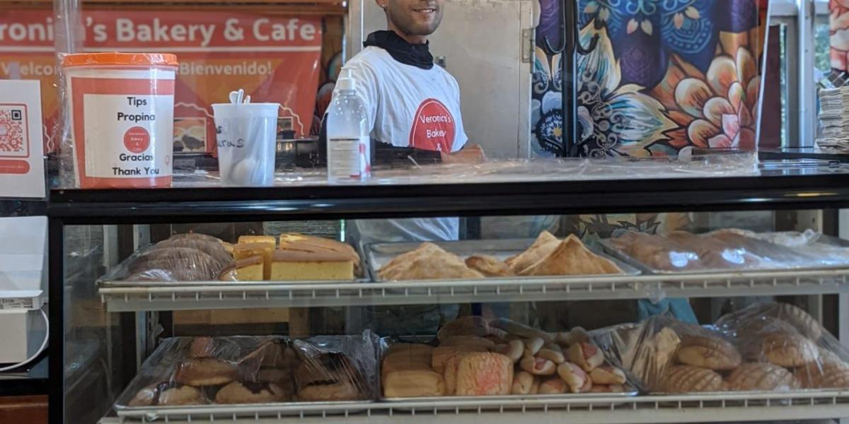 An employee behind a display case filled with bakery items.
