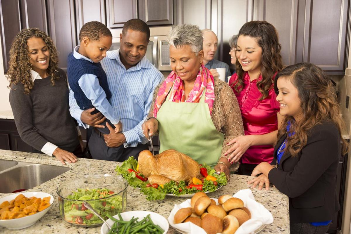 A smiling family collected around a Thanksgiving turkey being carved