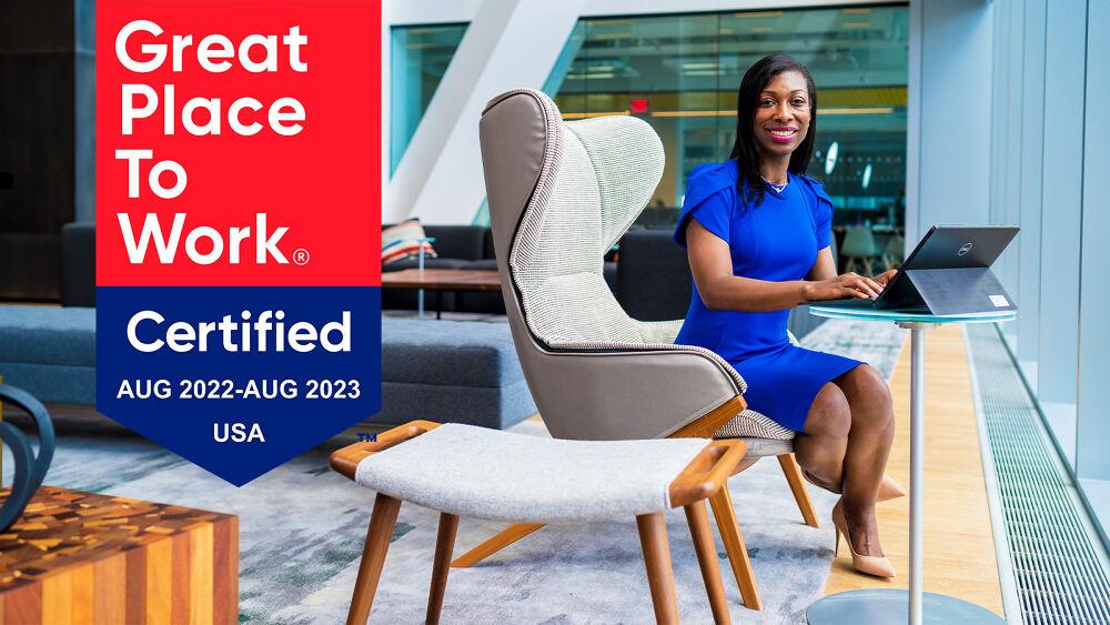 Woman sitting at a table with laptop with Great Place to Work Logo 