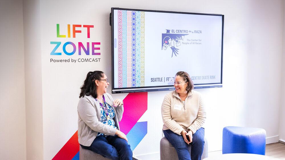 Two people sitting and talking in front of a mural that reads "Lift Zone, Powered by COMCAST"