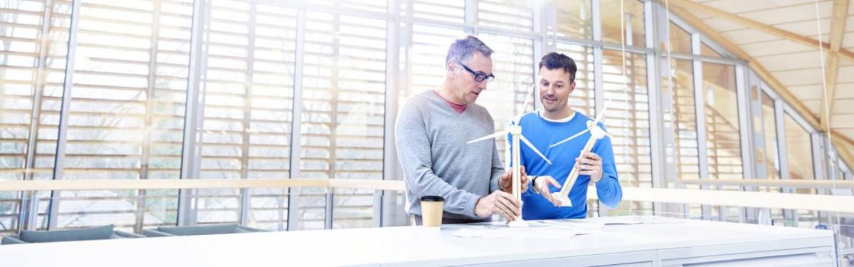 Two people holding small models of wind turbines in an open space.