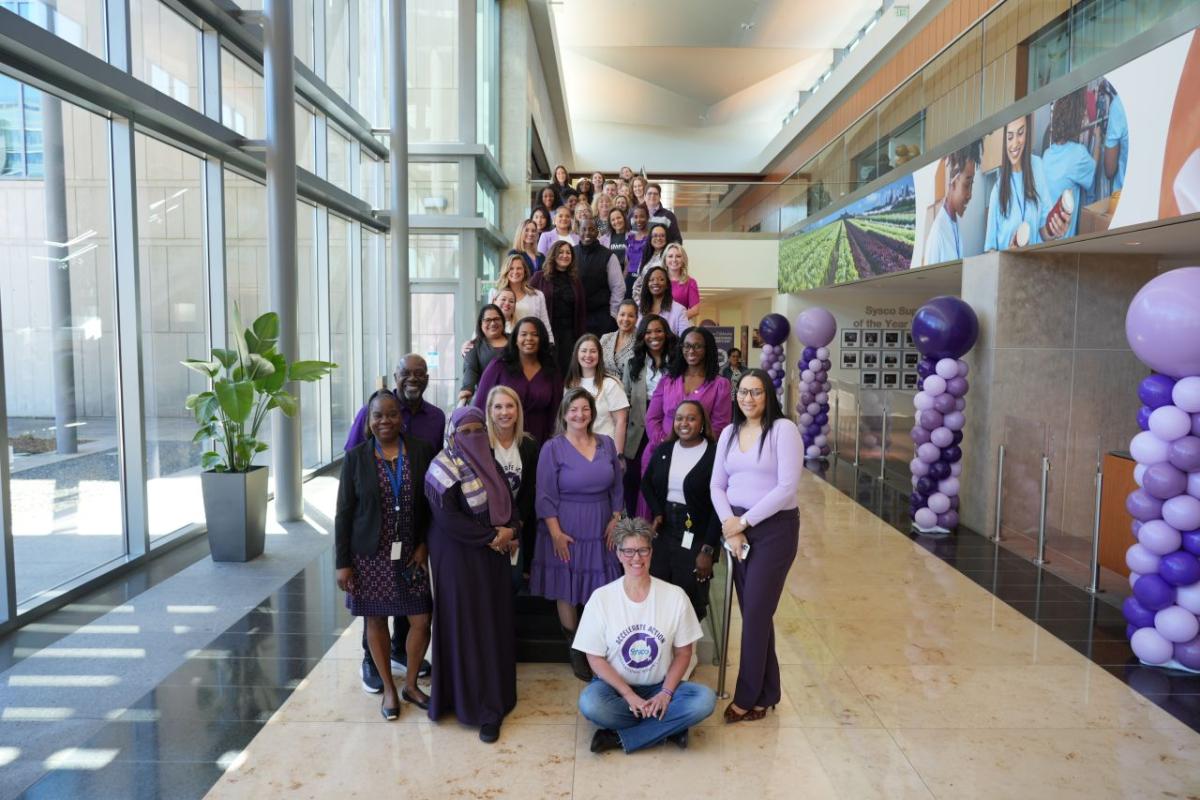 A group of people posed next to purple balloons and big windows